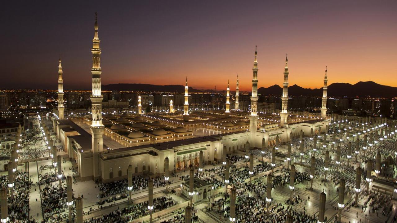 Hotel Intercontinental Dar Al Iman Madinah By Ihg Medina Exterior foto The photo depicts an aerial view of a large mosque complex during sunset. The mosque features multiple tall minarets, which are intricately designed and illuminated, giving the scene a stunning appearance as the sky transitions from daylight to dusk.