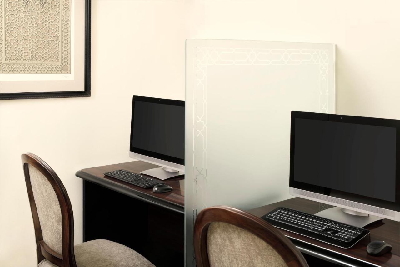 Hotel Intercontinental Dar Al Iman Madinah By Ihg Medina Exterior foto The photo shows a workspace featuring two computers set up on a dark wooden desk. Each computer has a monitor and a keyboard. A frosted glass partition is placed between the two workstations, providing some privacy. In the background, there is a fram