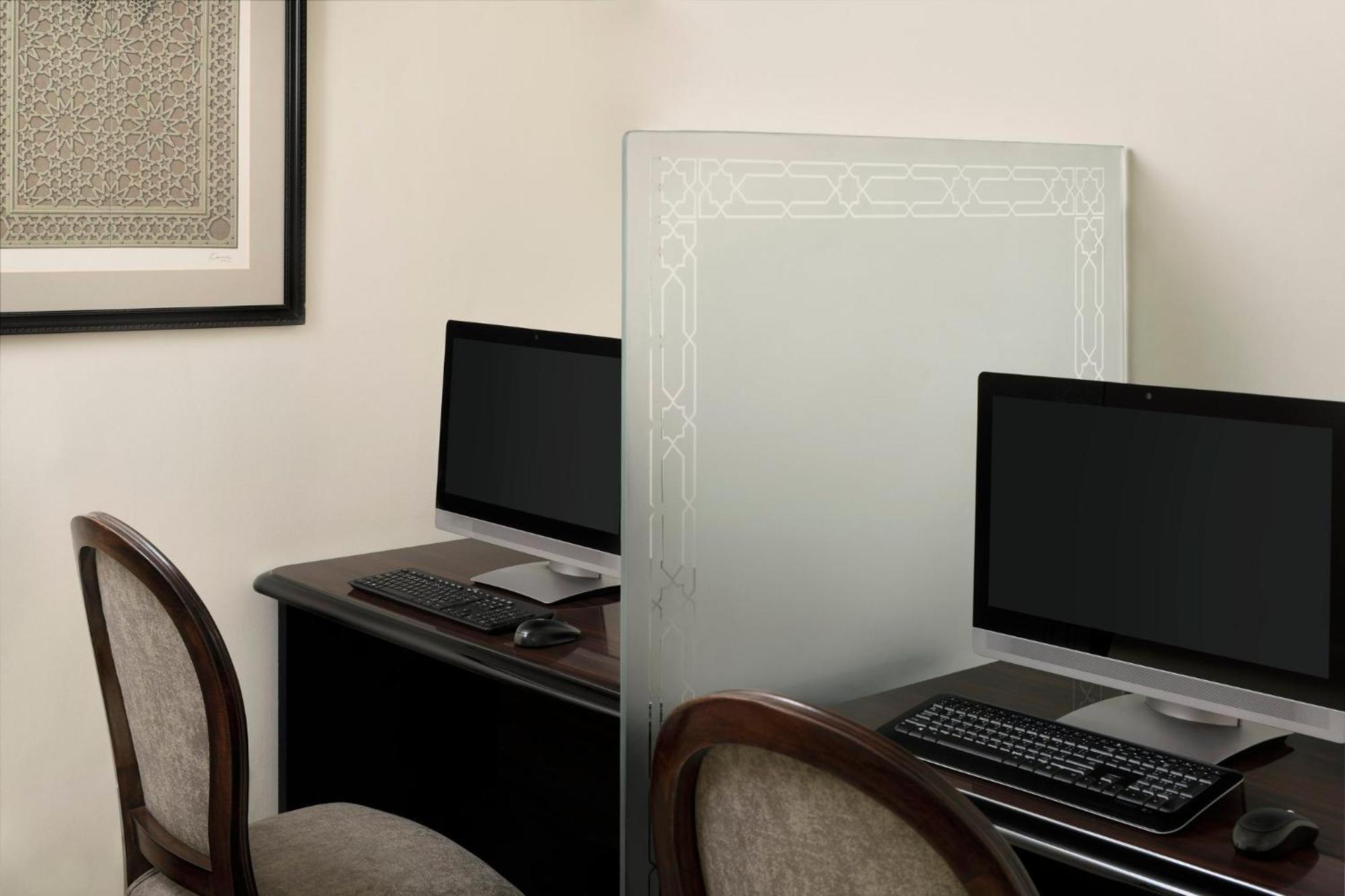 Hotel Intercontinental Dar Al Iman Madinah By Ihg Medina Exterior foto The photo shows a small office or workspace area featuring two computer stations. Each station has a black monitor, a keyboard, and appears to be set up on a dark wooden desk. A translucent glass partition is placed between the two workstations, prov