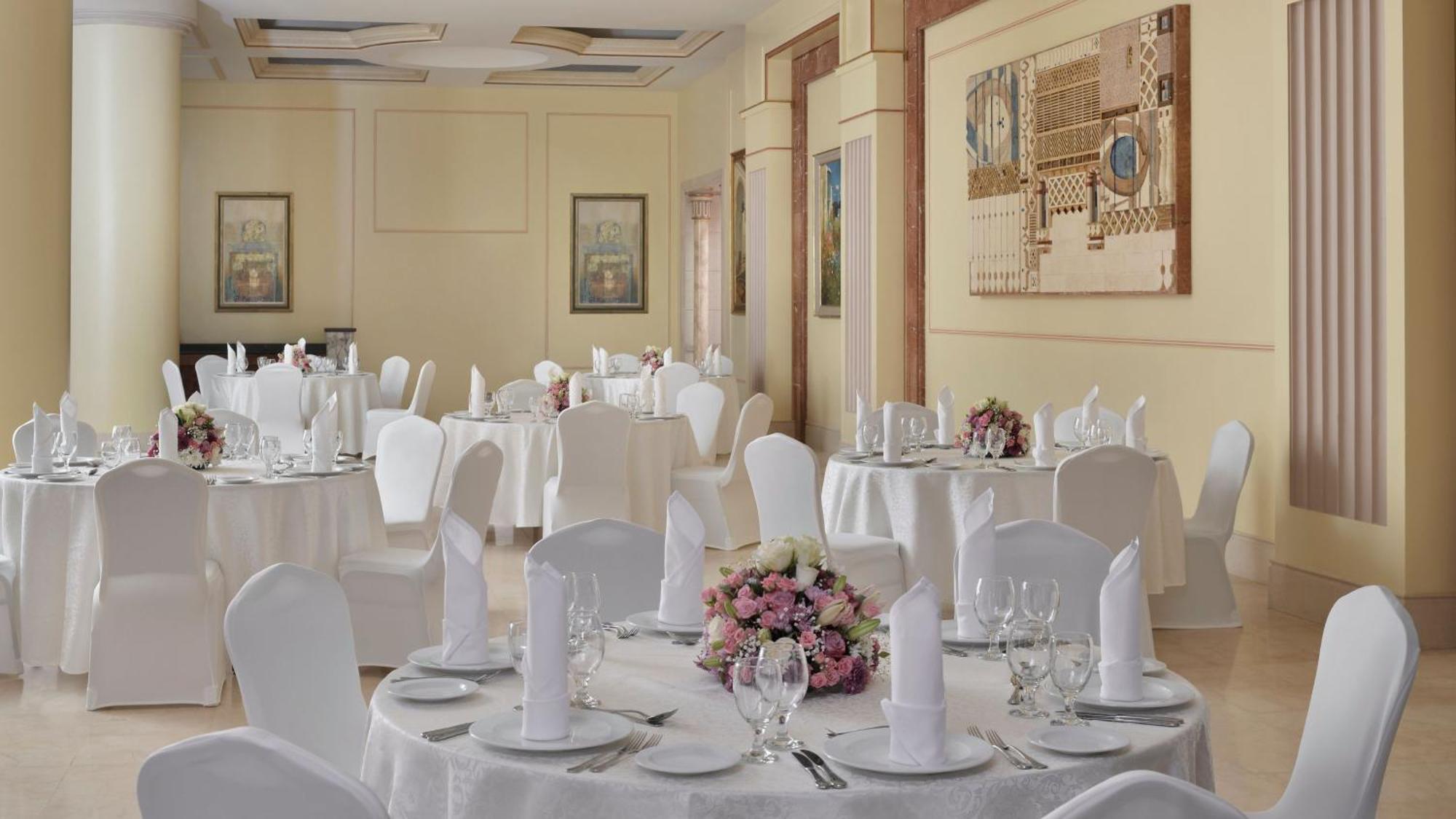 Hotel Intercontinental Dar Al Iman Madinah By Ihg Medina Exterior foto The photo shows an elegantly arranged dining area, likely set up for a formal event or reception. There are several round tables covered with white tablecloths, each adorned with floral centerpieces featuring pink flowers. The tables are set with pla
