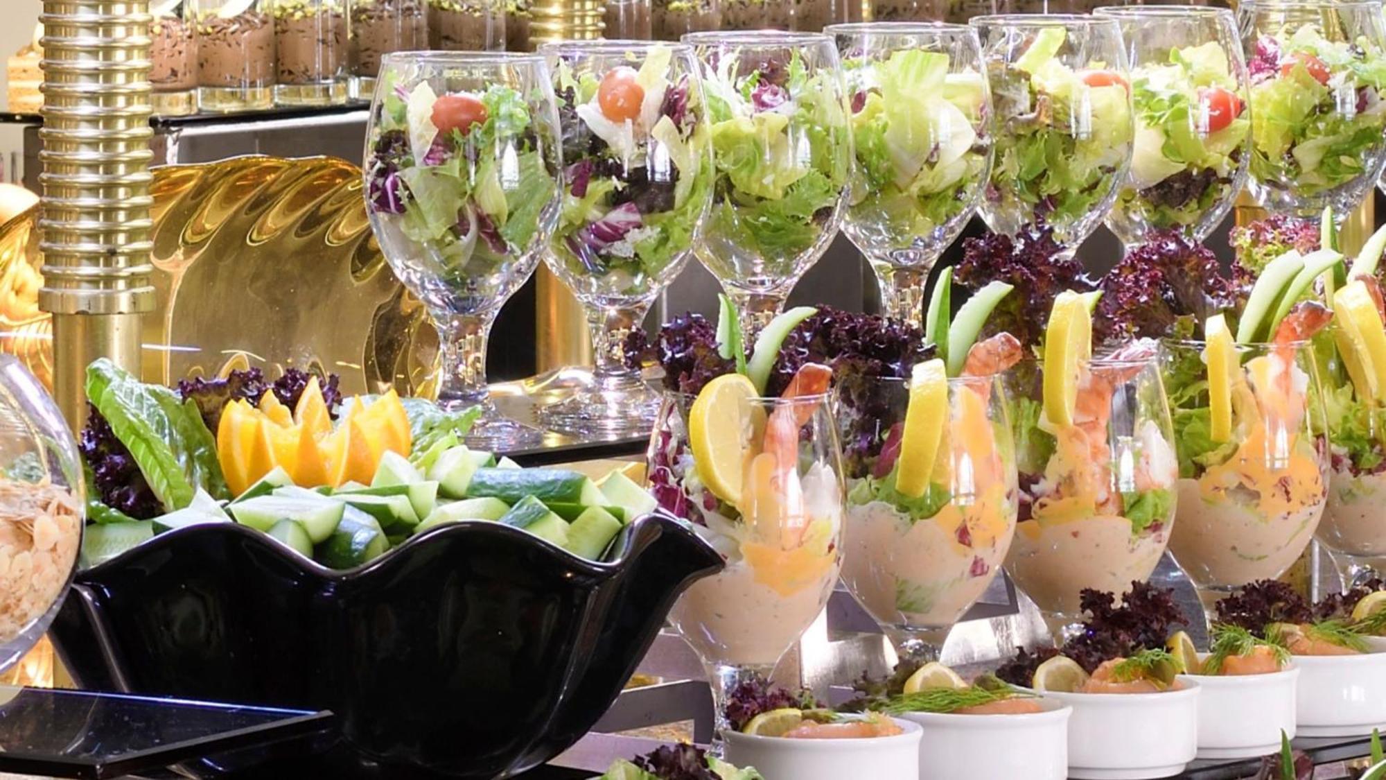 Hotel Intercontinental Dar Al Iman Madinah By Ihg Medina Exterior foto The photo features an elegant display of food items. In the background, there are several clear glasses filled with vibrant salads, featuring various types of greens and garnishes. In the foreground, there is a decorative black bowl containing cut pi
