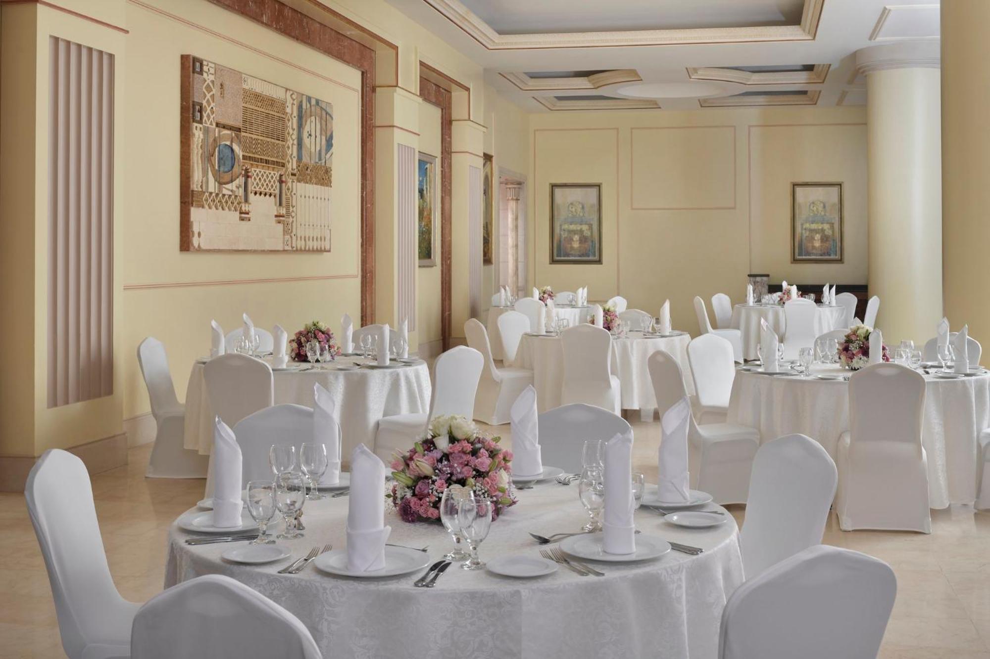 Hotel Intercontinental Dar Al Iman Madinah By Ihg Medina Exterior foto The photo shows an elegantly arranged dining or function room. There are round tables covered with white tablecloths, each set with fine dining ware including glassware, utensils, and neatly folded white napkins. Some tables have floral centerpieces 