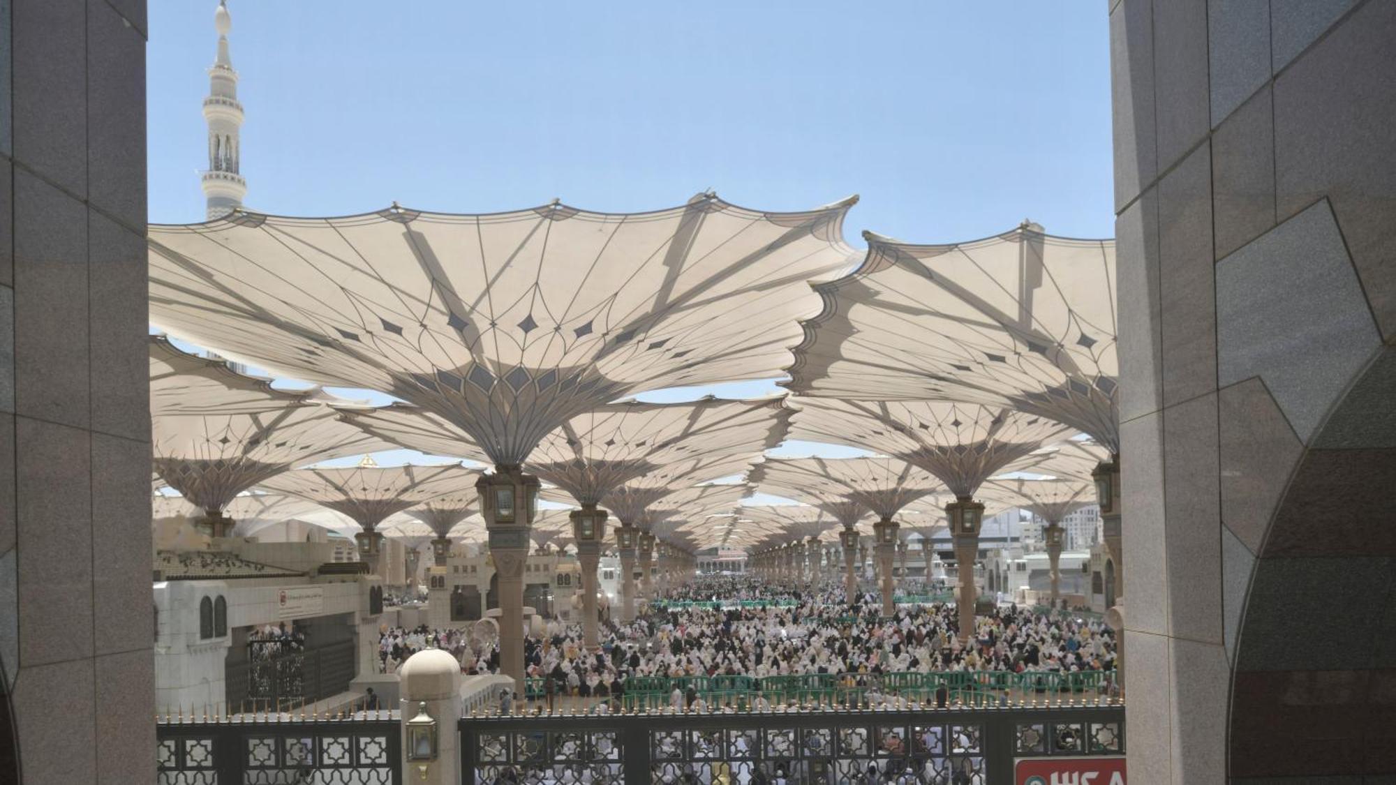 Hotel Intercontinental Dar Al Iman Madinah By Ihg Medina Exterior foto The photo shows a large open area covered by expansive canopies, likely designed to provide shade for the people below. Underneath the canopies, there are many individuals gathered, possibly participating in a religious event or gathering. In the bac