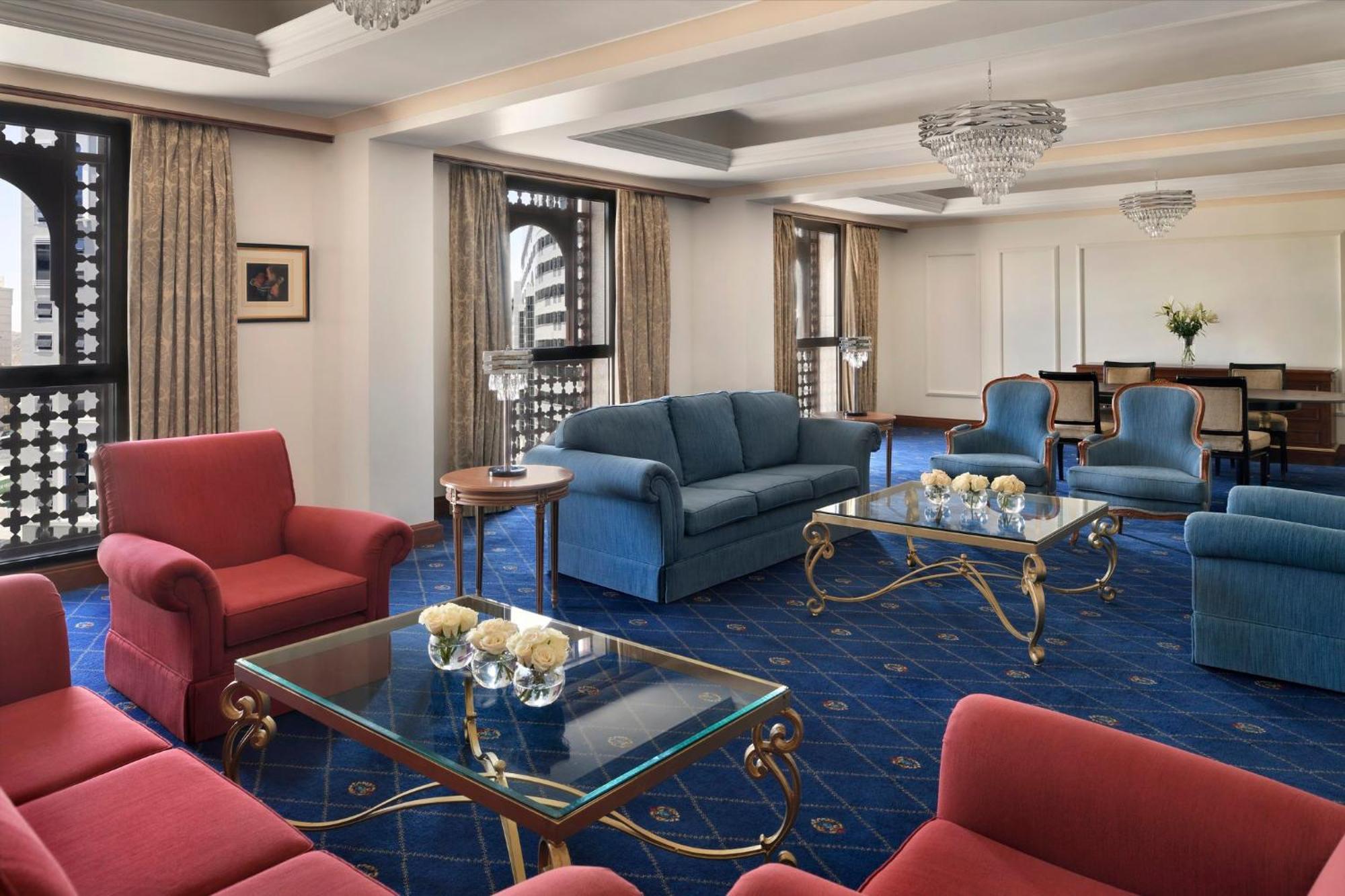 Hotel Intercontinental Dar Al Iman Madinah By Ihg Medina Exterior foto The photo shows a luxurious living space or lounge area. It features a combination of furniture, including a blue sofa, several red armchairs, and glass-top coffee tables with gold accents. The flooring is carpeted in a deep blue, and the walls are a