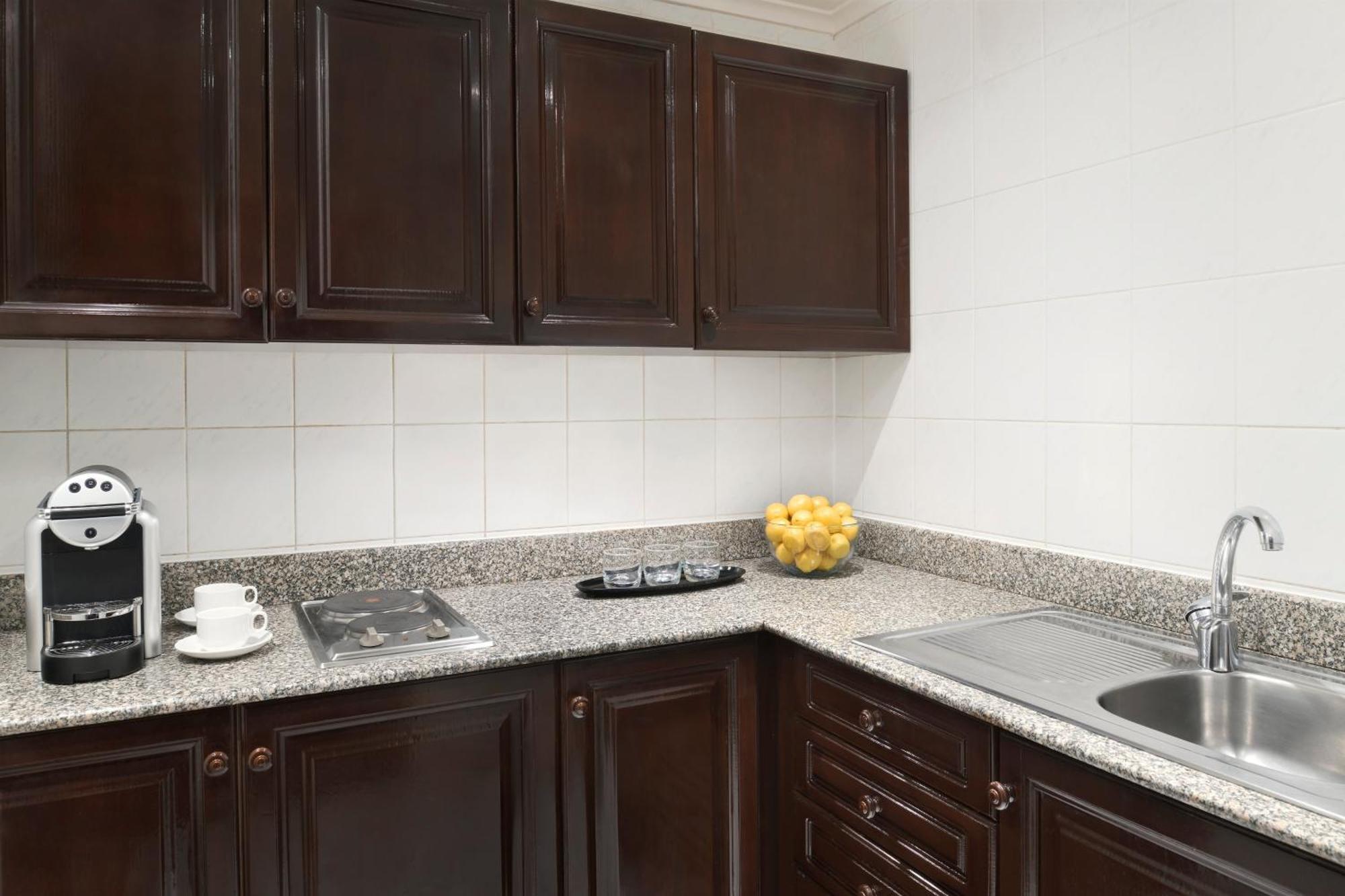 Hotel Intercontinental Dar Al Iman Madinah By Ihg Medina Exterior foto The photo shows a kitchen with dark wooden cabinetry and a light-colored countertop. There are a few appliances visible, including a coffee machine and a stovetop with burners. To the right, there is a sink, and a bowl of yellow lemons is placed on t