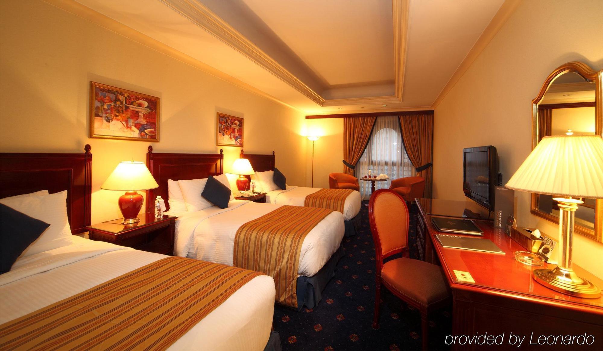Hotel Intercontinental Dar Al Iman Madinah By Ihg Medina Habitación foto The photo shows a hotel room with a warm and inviting atmosphere. There are two beds with white and gold bedding, complemented by decorative pillows. Each bed has a bedside lamp. In the background, there's a small seating area with a couple of chairs