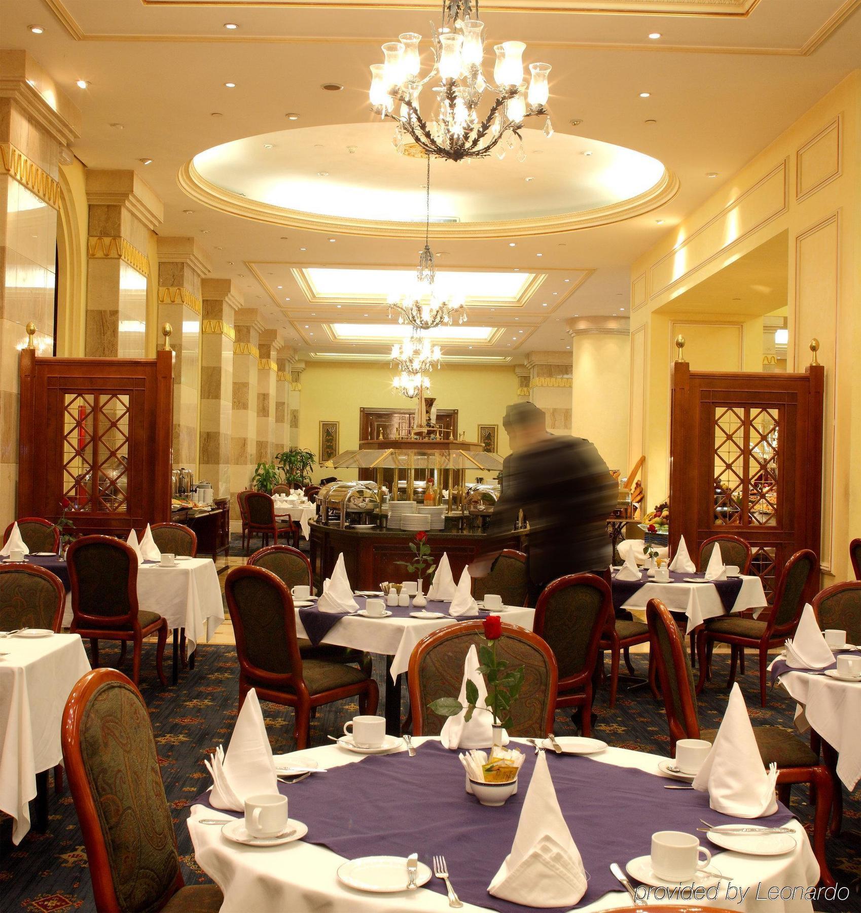 Hotel Intercontinental Dar Al Iman Madinah By Ihg Medina Restaurante foto The photo depicts an elegant restaurant interior. It features round tables covered with white tablecloths, each set with plates, cutlery, and folded napkins arranged into triangles. The space has a warm, inviting atmosphere with a mix of decorative e